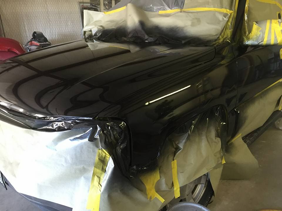 A black car is being painted in a garage