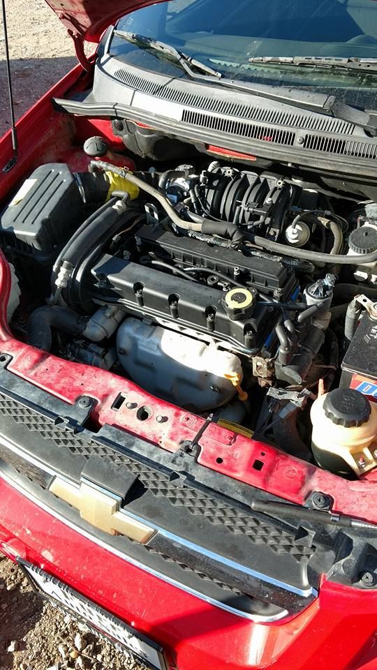 The engine of a red car is shown with the hood open.