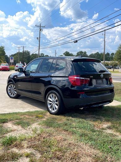 Black BMW X3 SUV parked on concrete next to grass; power lines and cloudy sky in background.