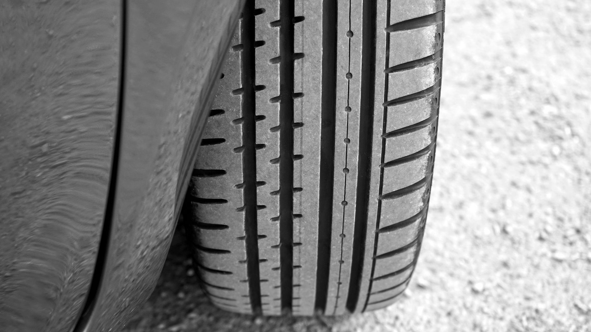 Black and white close-up of a car tire with tread lines on asphalt.