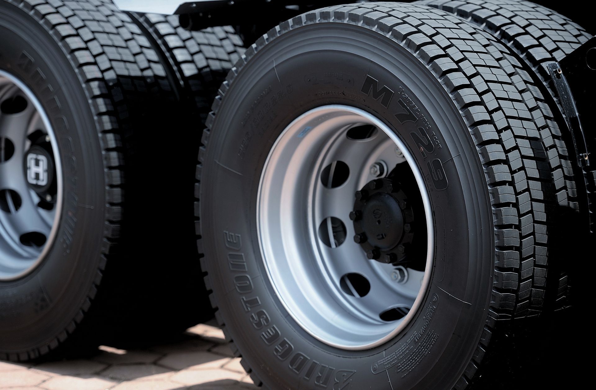 Close-up of a semi-truck's rear tires, silver rims, black tires, on a dark surface.