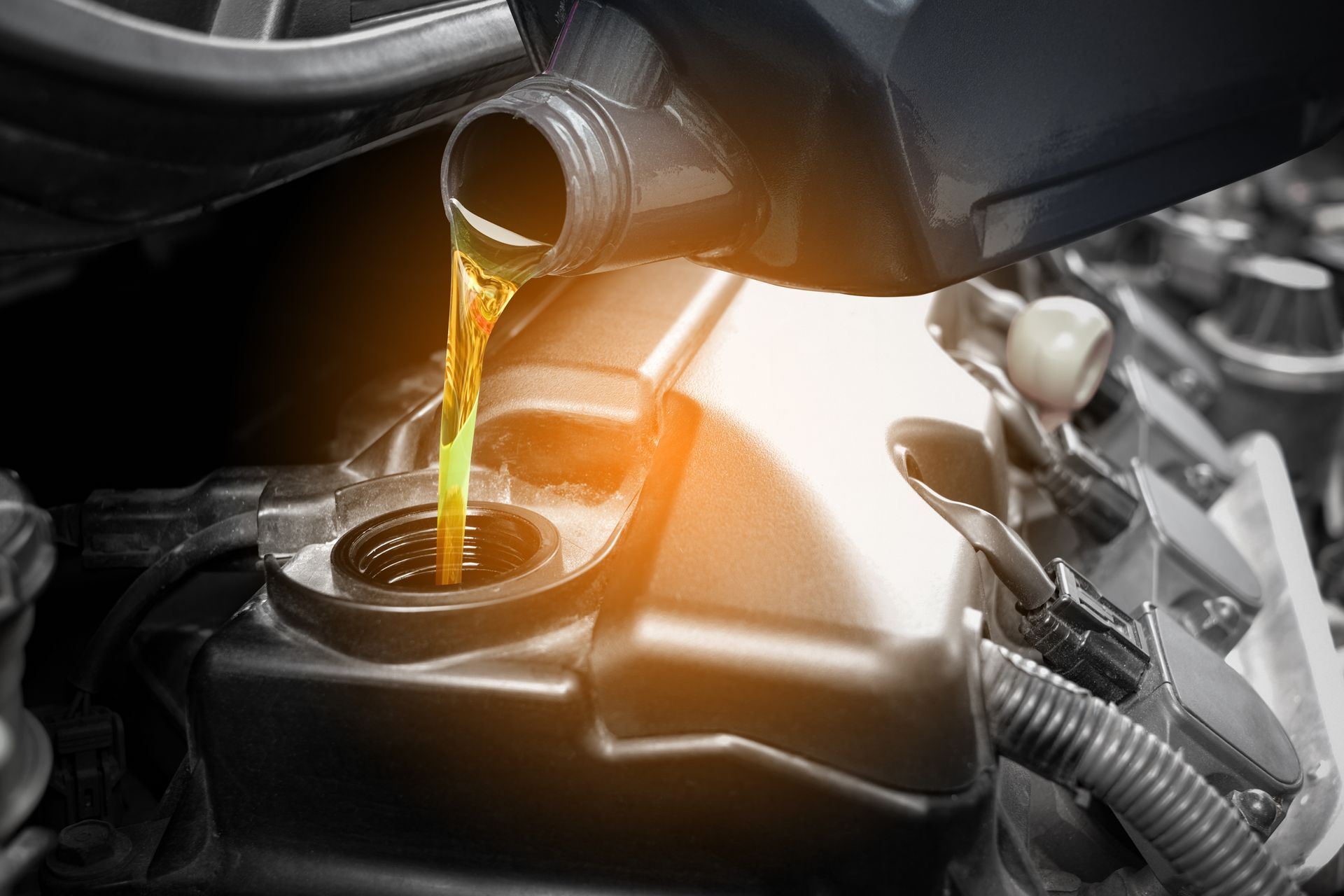 Pouring oil into a car engine. Yellow oil flows from a black container.