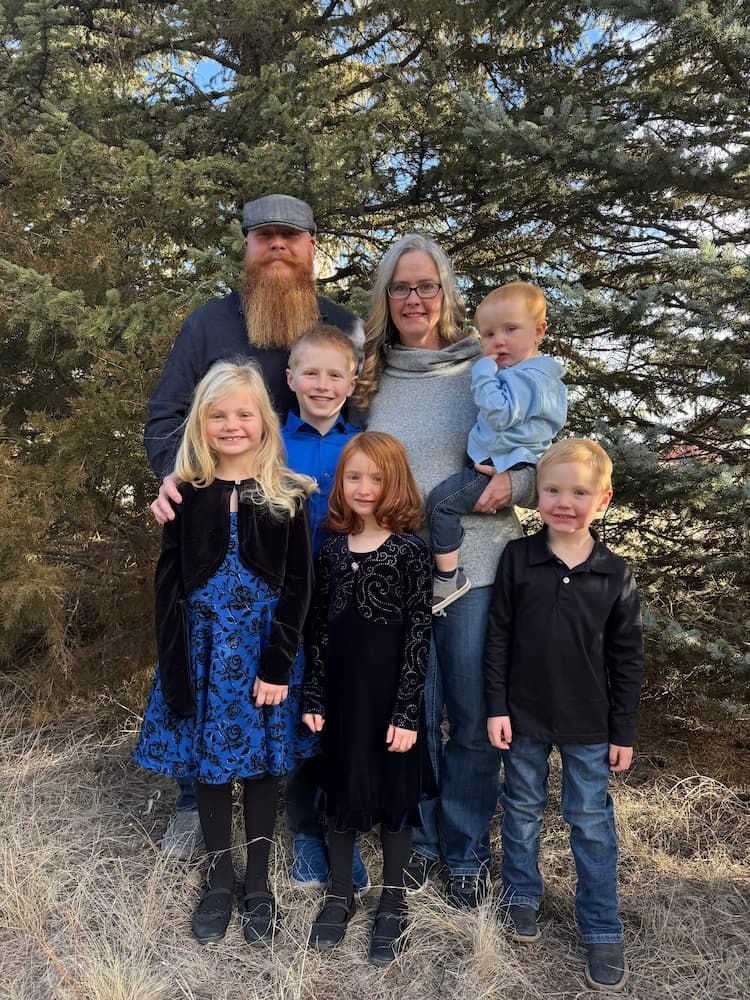 A family is posing for a picture in front of a pine tree.