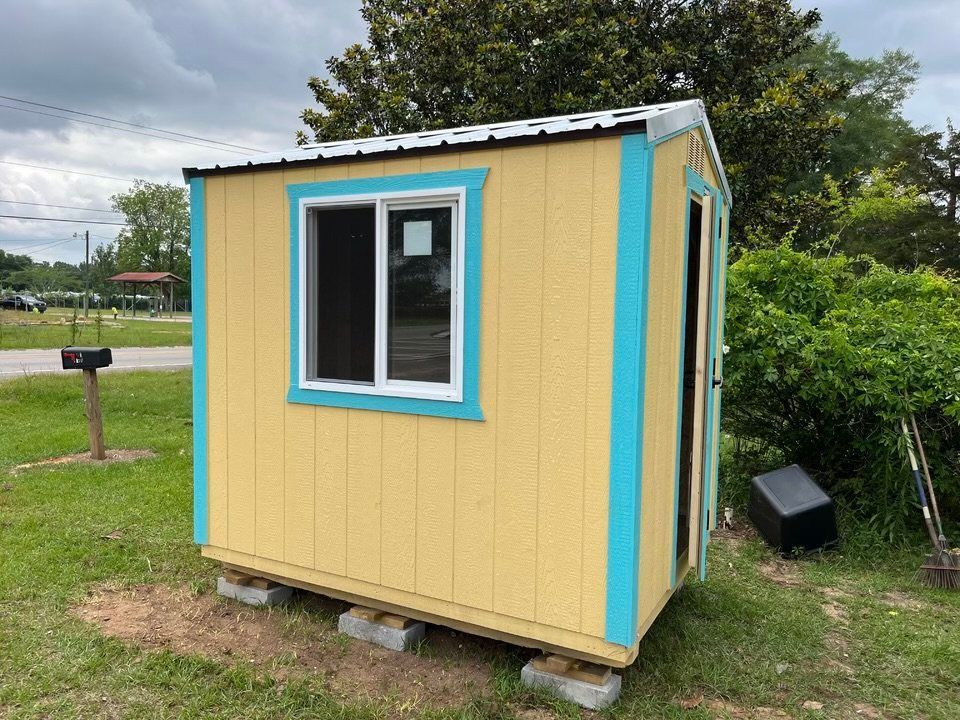 A small yellow and blue shed with a window is sitting in the grass.