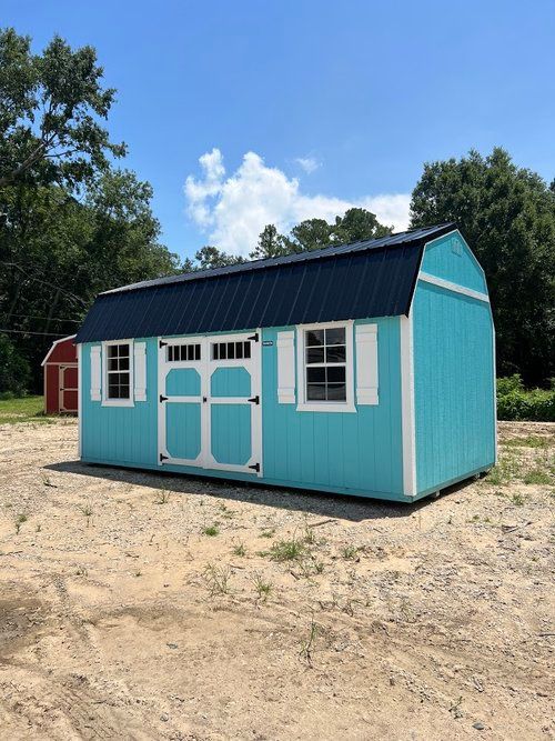 A blue barn with white shutters is sitting in a dirt field.
