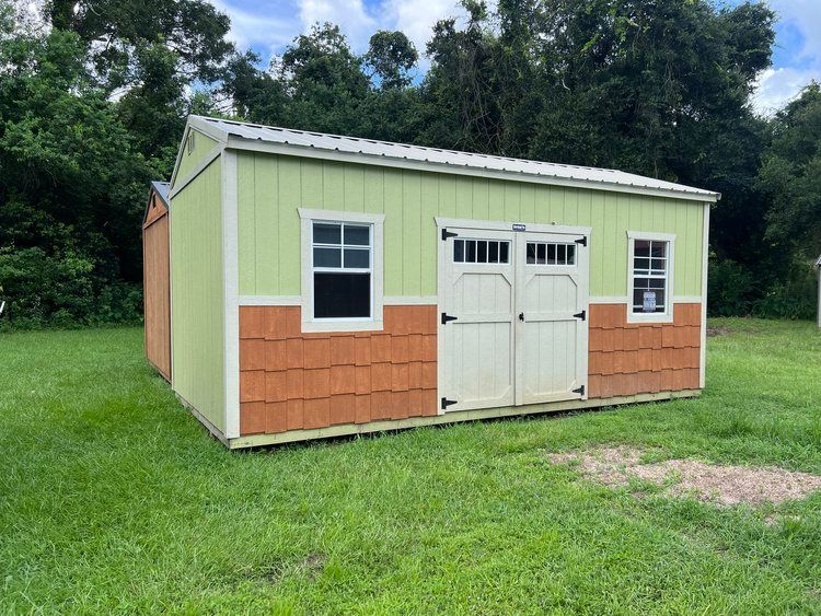 A green and orange shed is sitting in the middle of a grassy field.