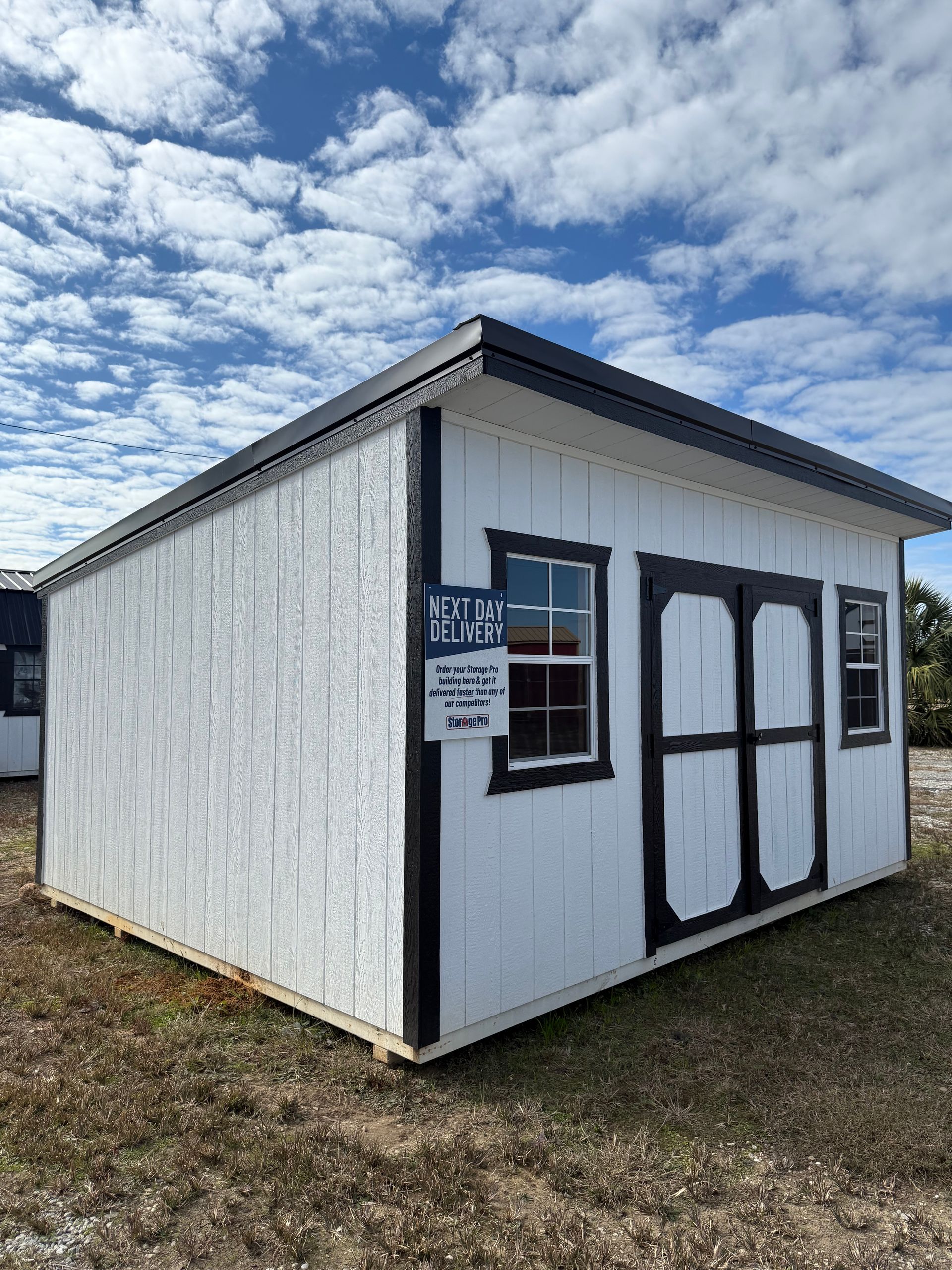 A small white shed with black trim is sitting in a field.