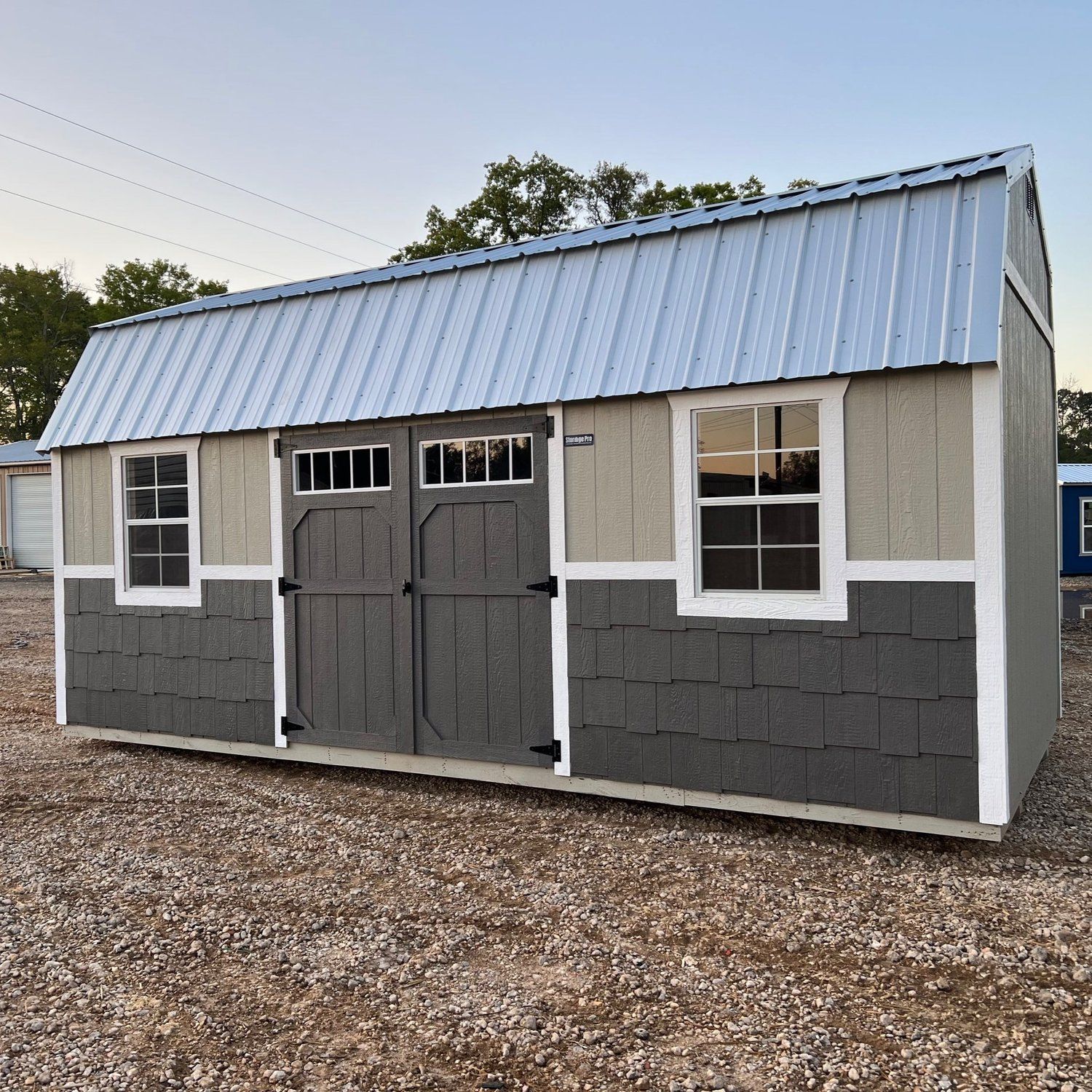 A shed with a metal roof is sitting in the dirt.