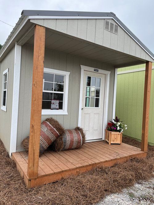 A small house with a porch and hay bales on the porch.