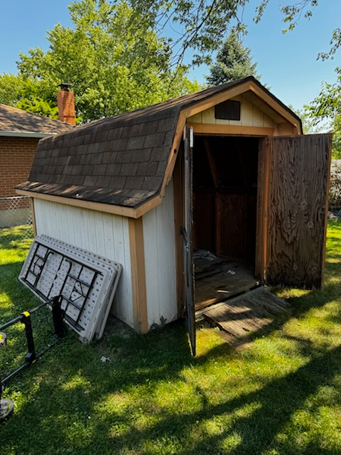 A white shed with a brown roof is sitting in the grass.