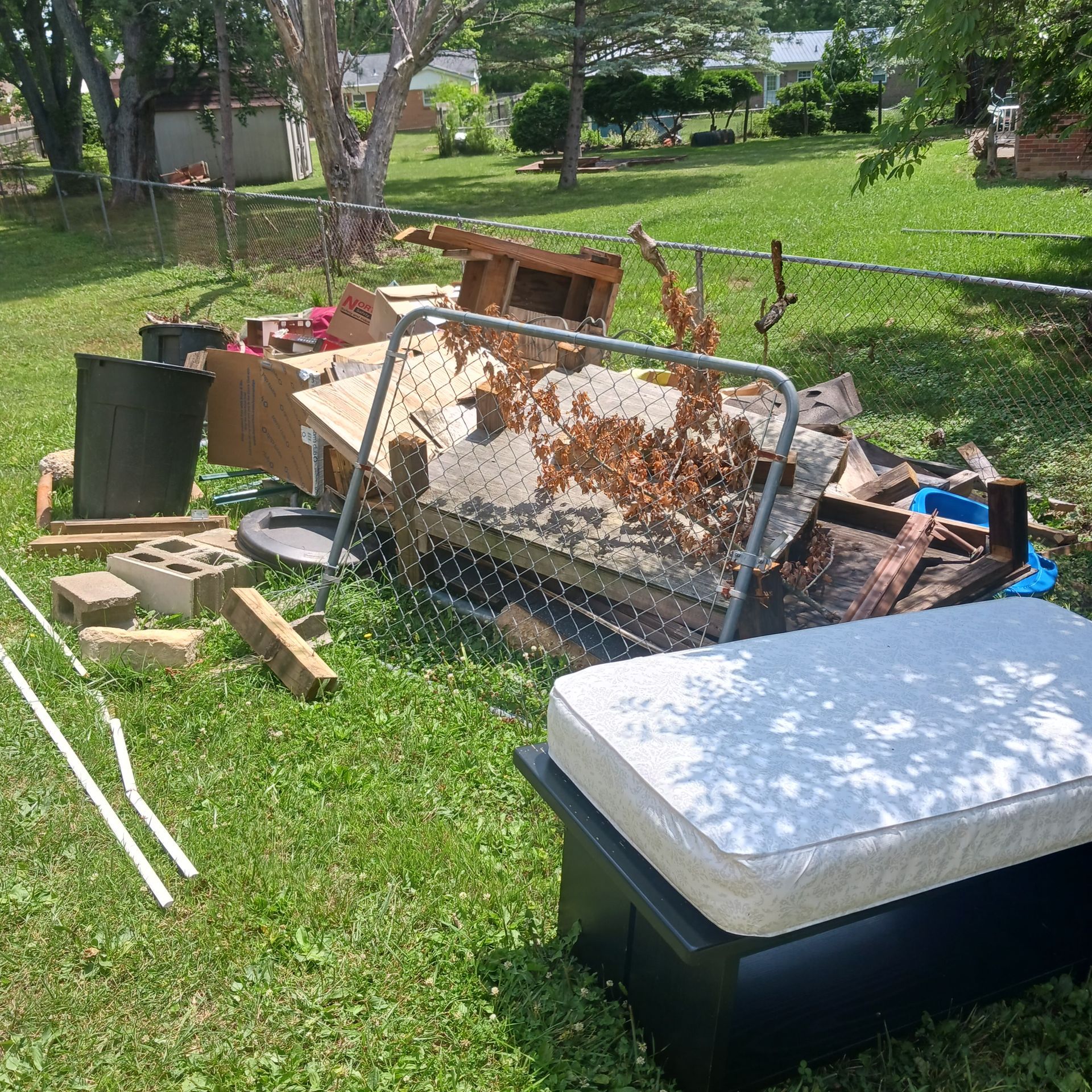 A mattress is sitting in the grass next to a fence