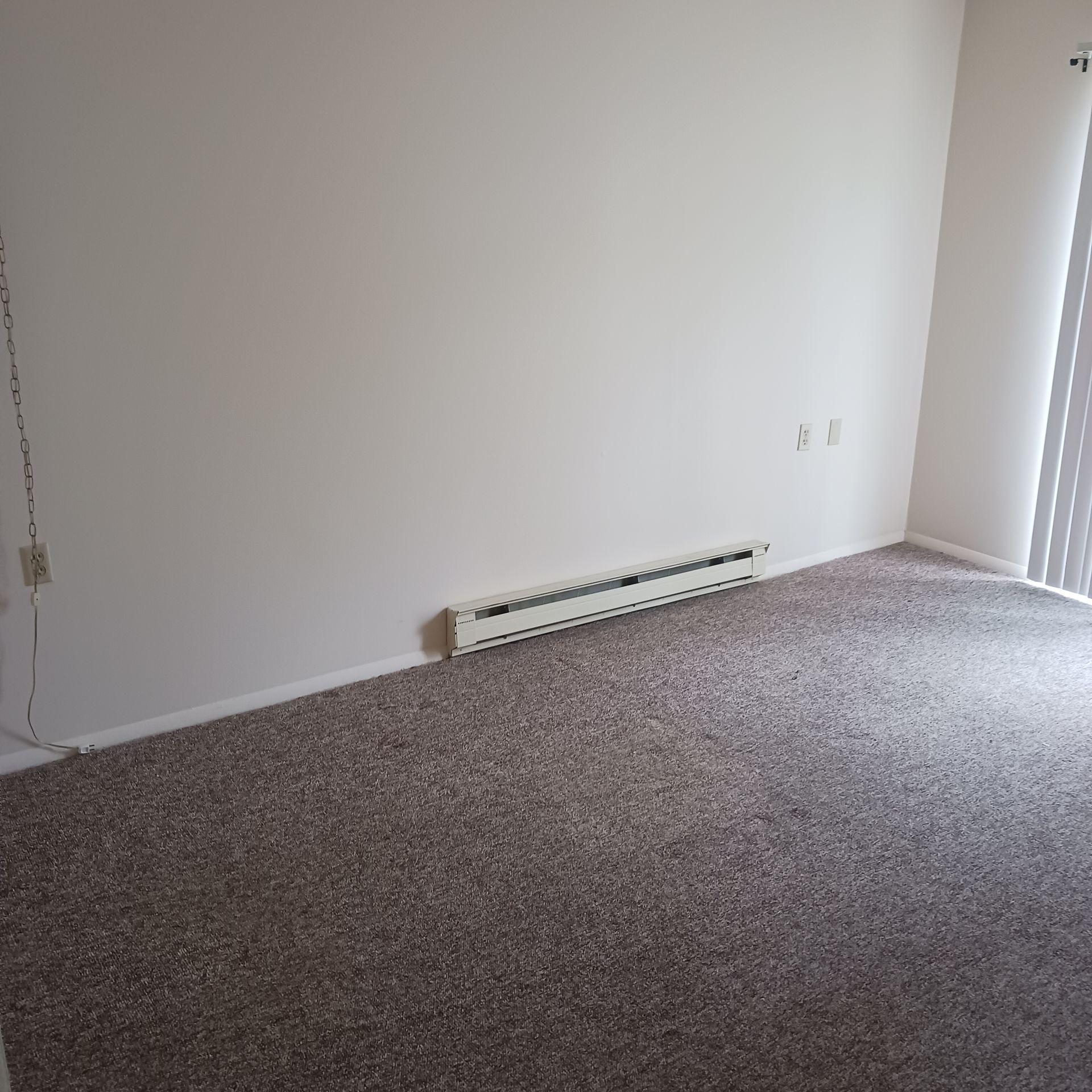An empty living room with a carpeted floor and white walls