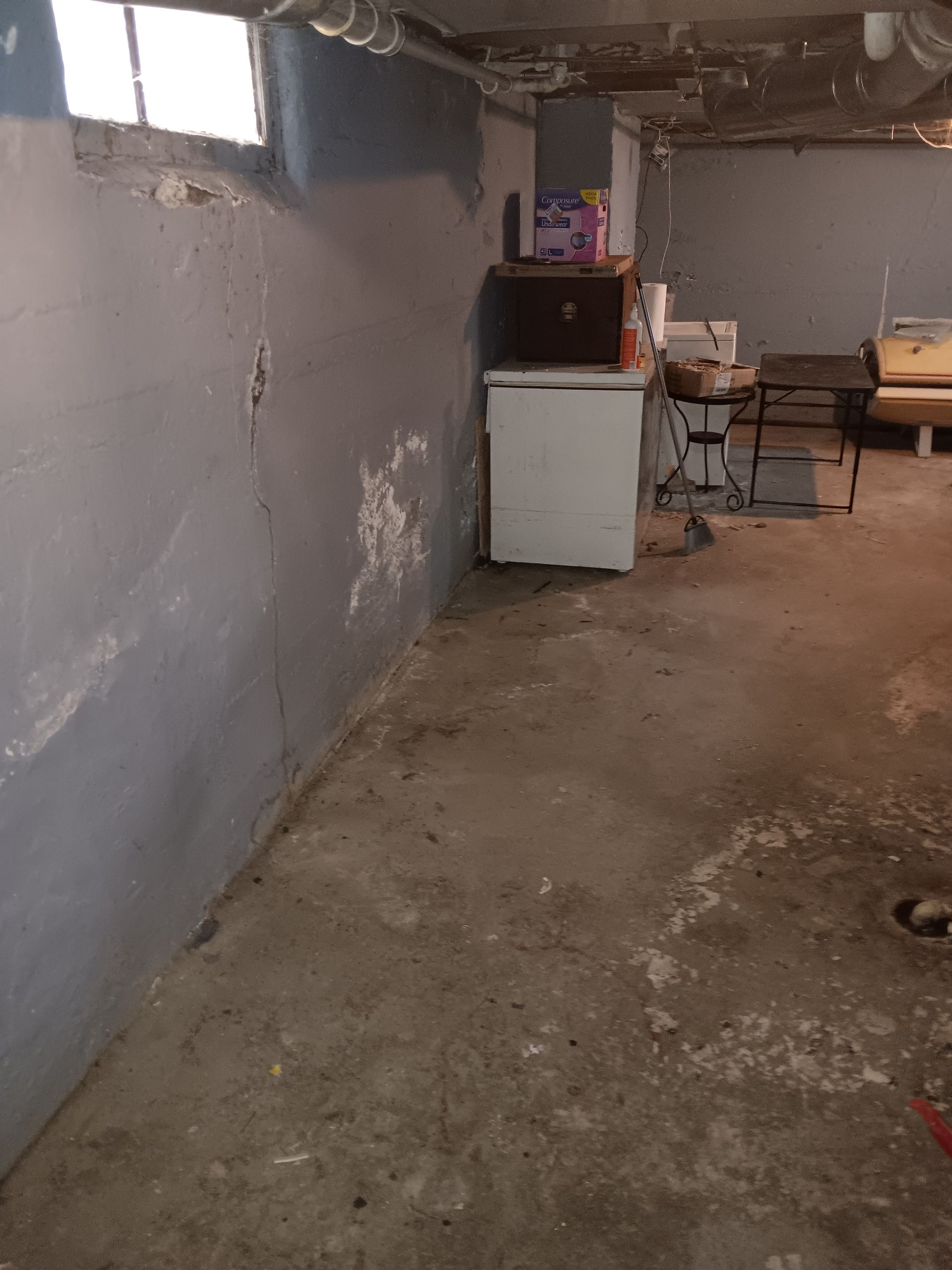 A dirty basement with a refrigerator and a sink.