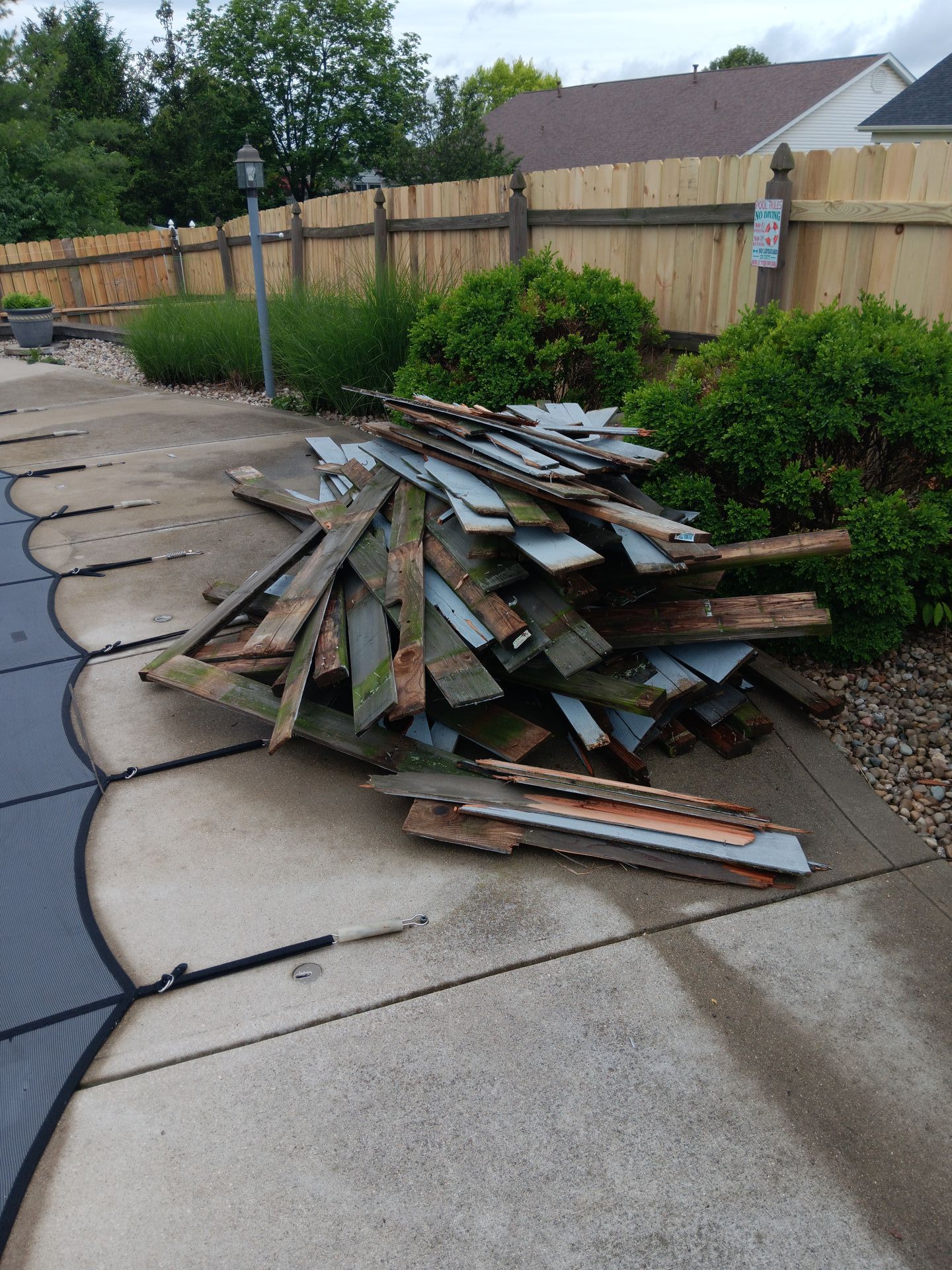 A pile of wood is sitting on the sidewalk next to a pool.