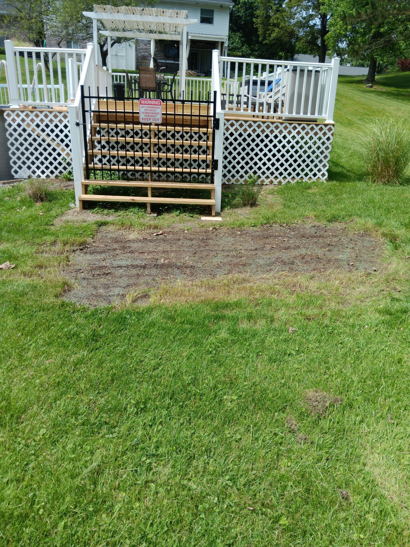 A deck with stairs leading up to it is in the middle of a lush green yard.