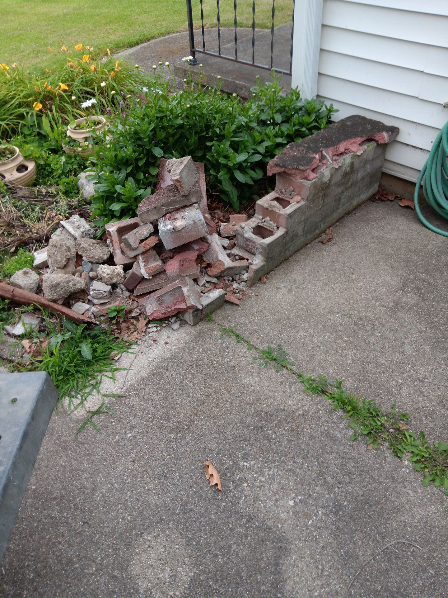 A pile of bricks is sitting on the sidewalk next to a hose.