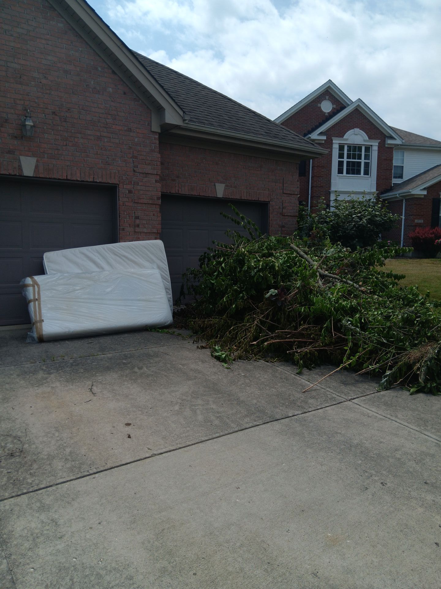 A mattress is sitting in a driveway in front of a brick house.