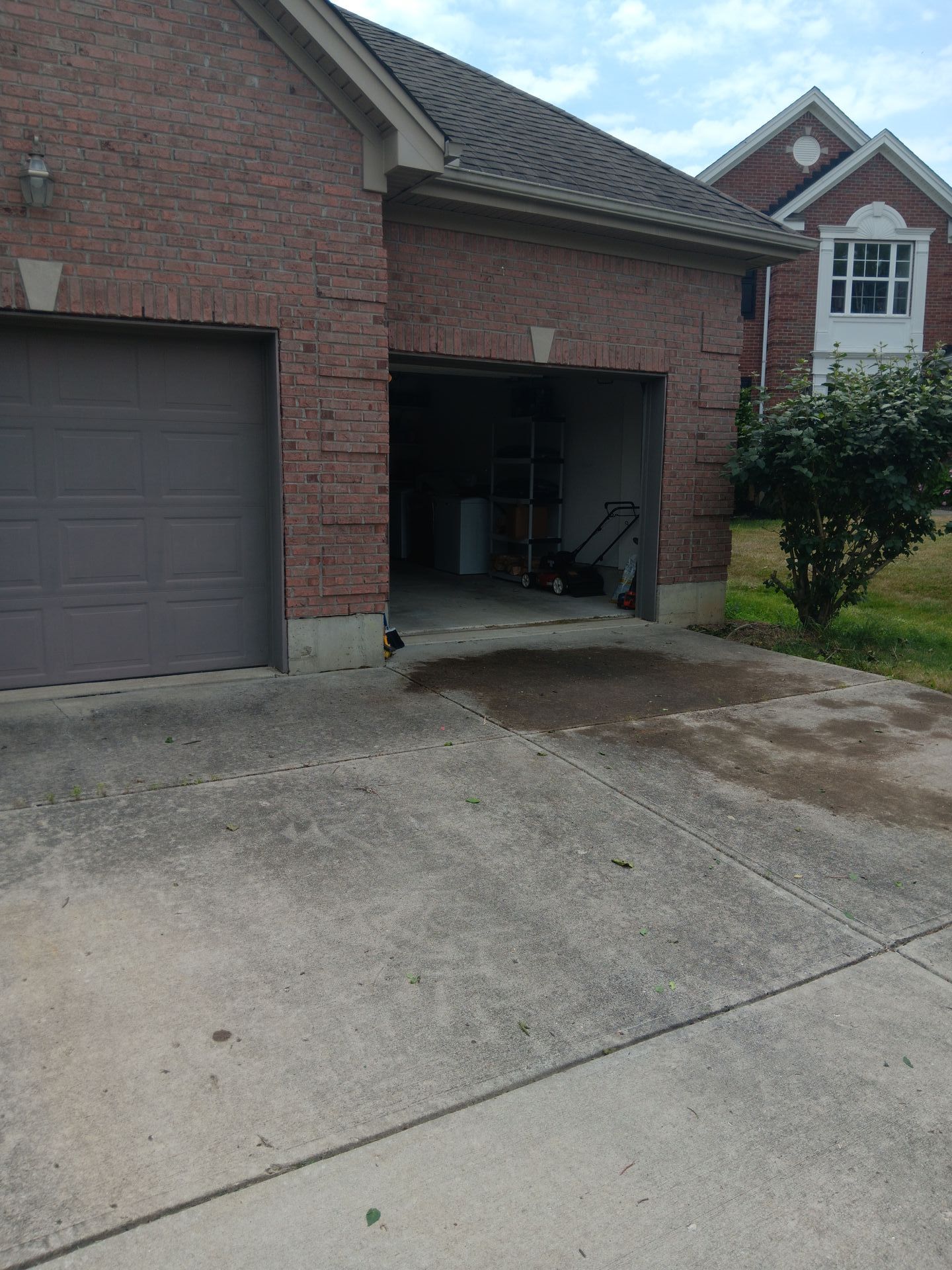 A brick house with two garage doors and a lawn mower in the driveway.