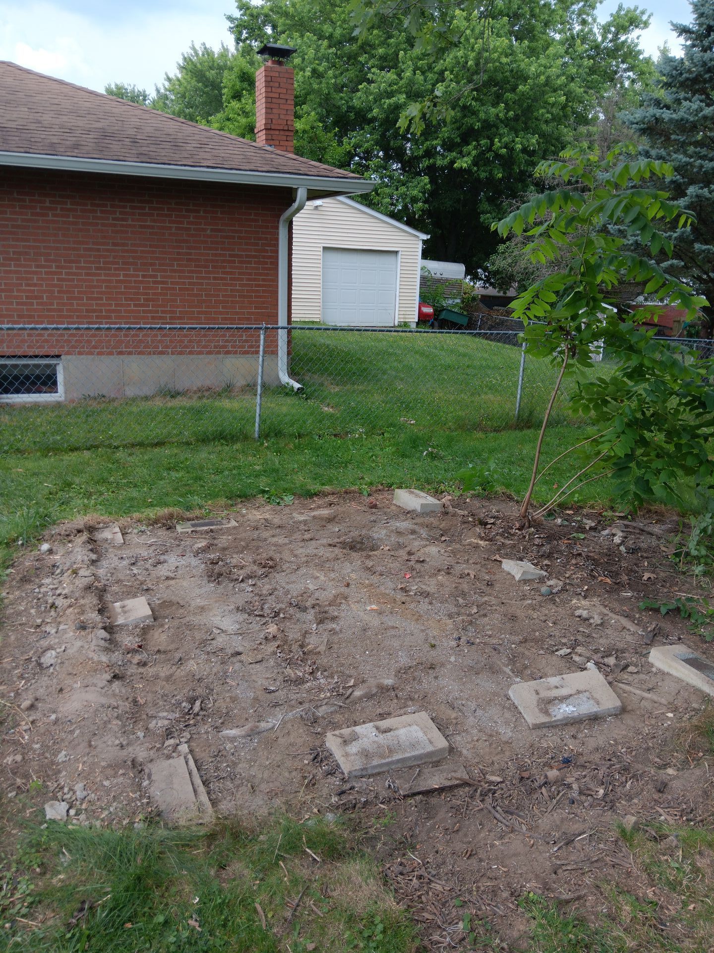 A dirt area in front of a brick house with a garage in the background.