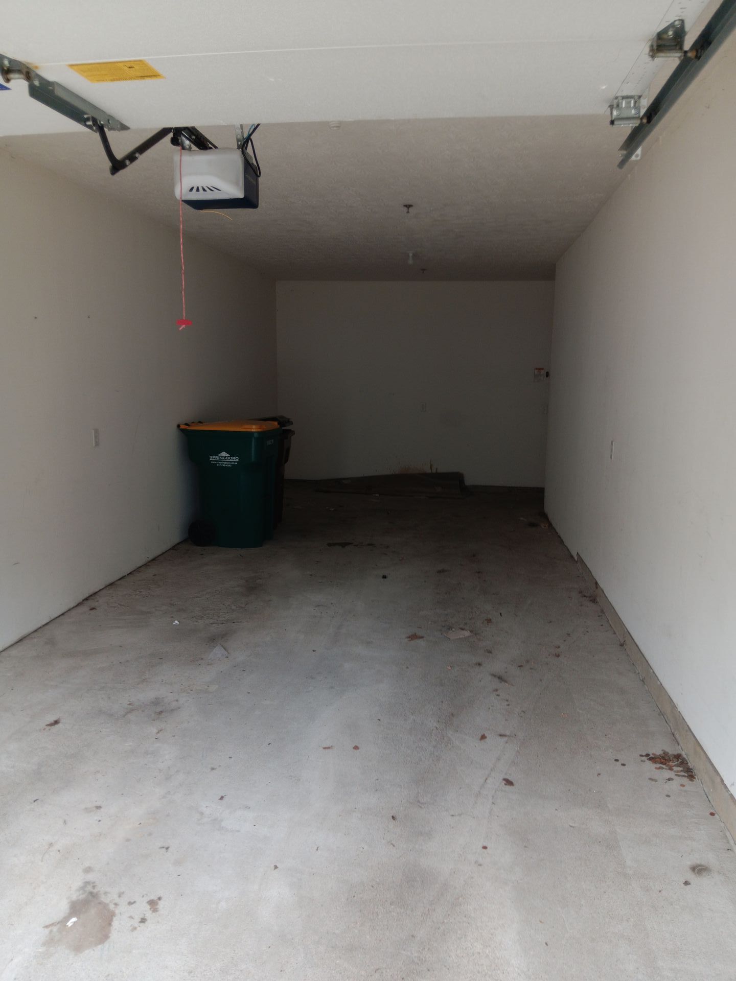 An empty garage with a green trash can and a garage door opener