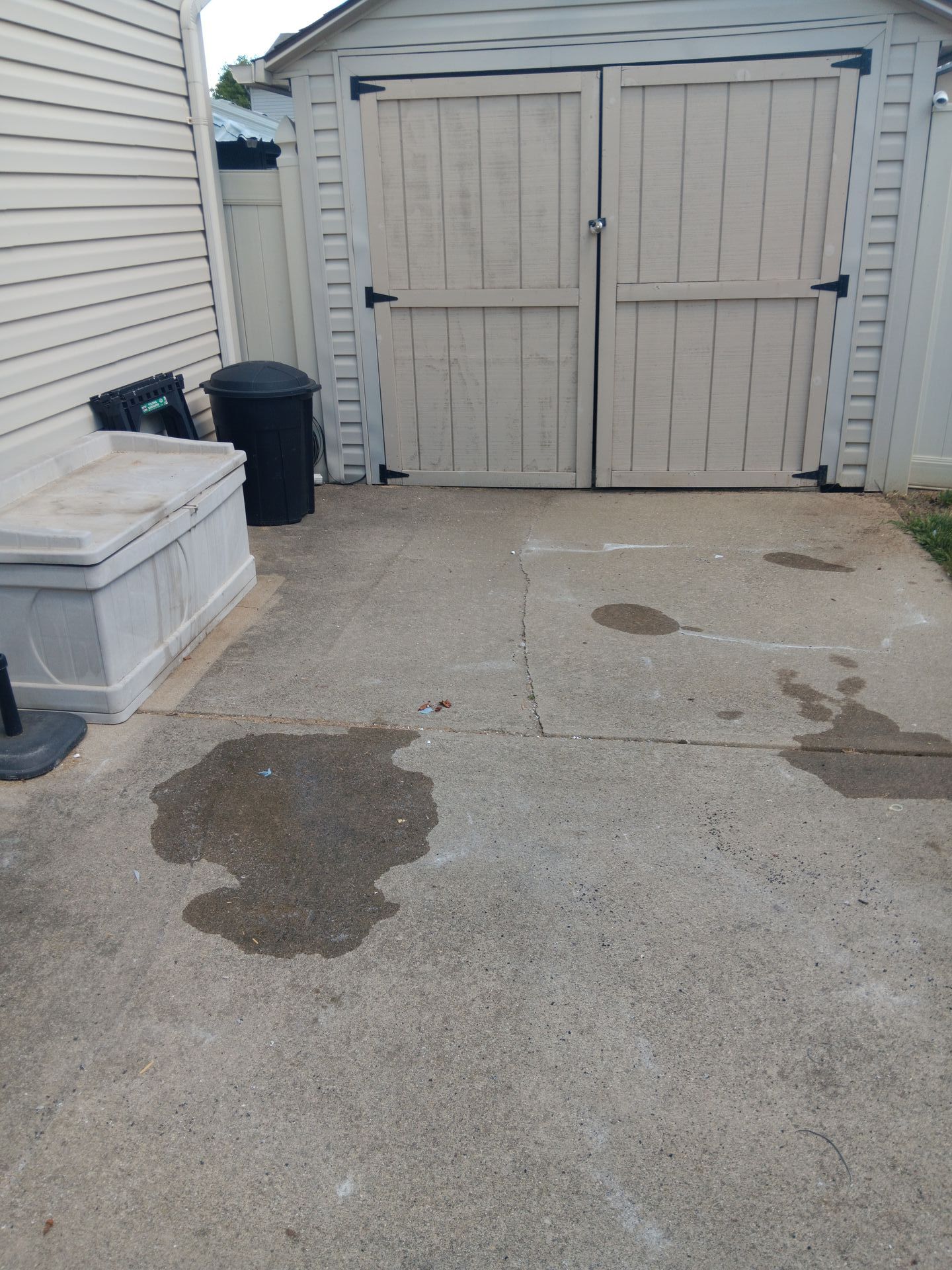 A white shed with a black trash can in front of it