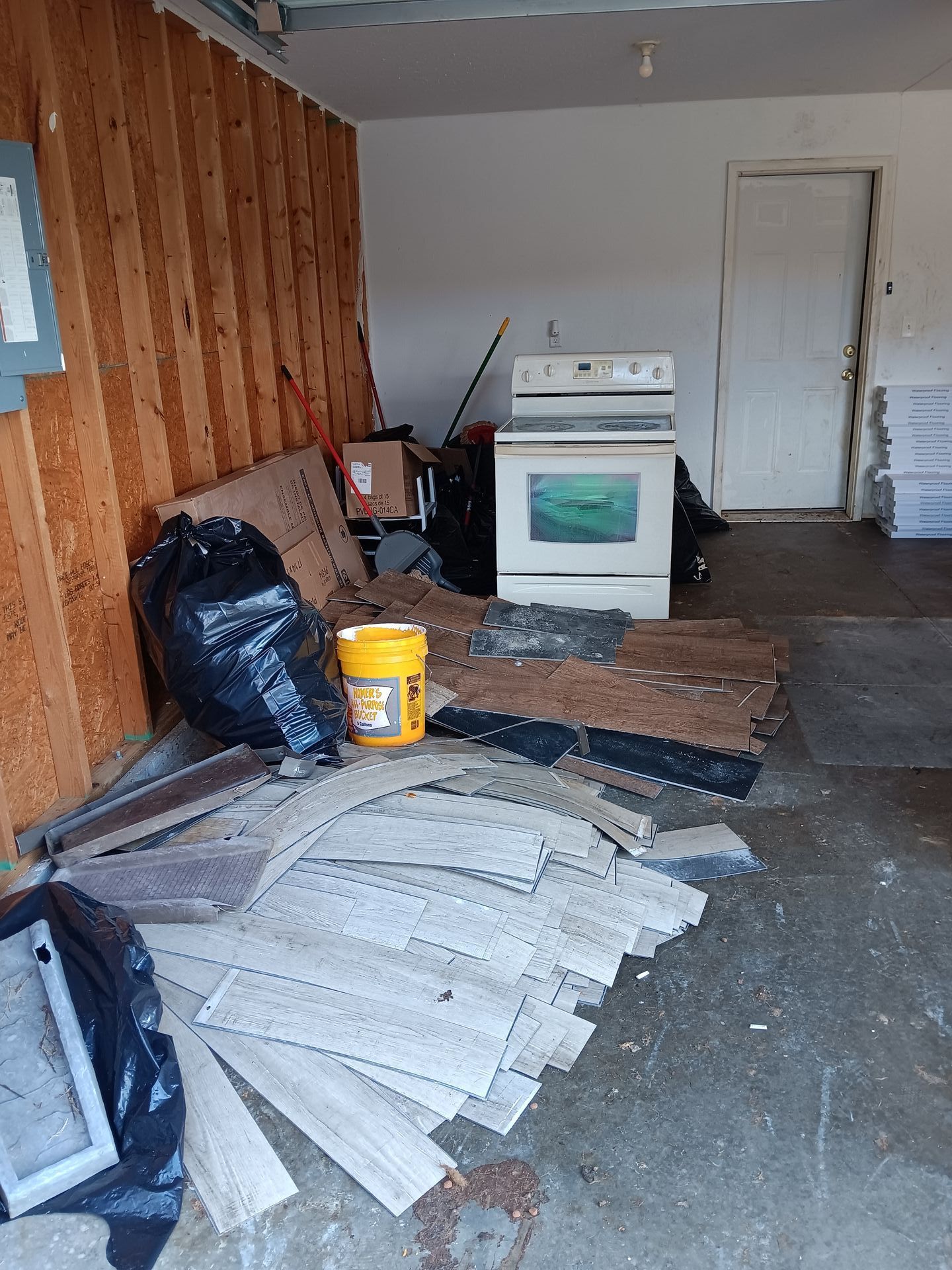 An empty garage with a stove and a yellow bucket on the floor.