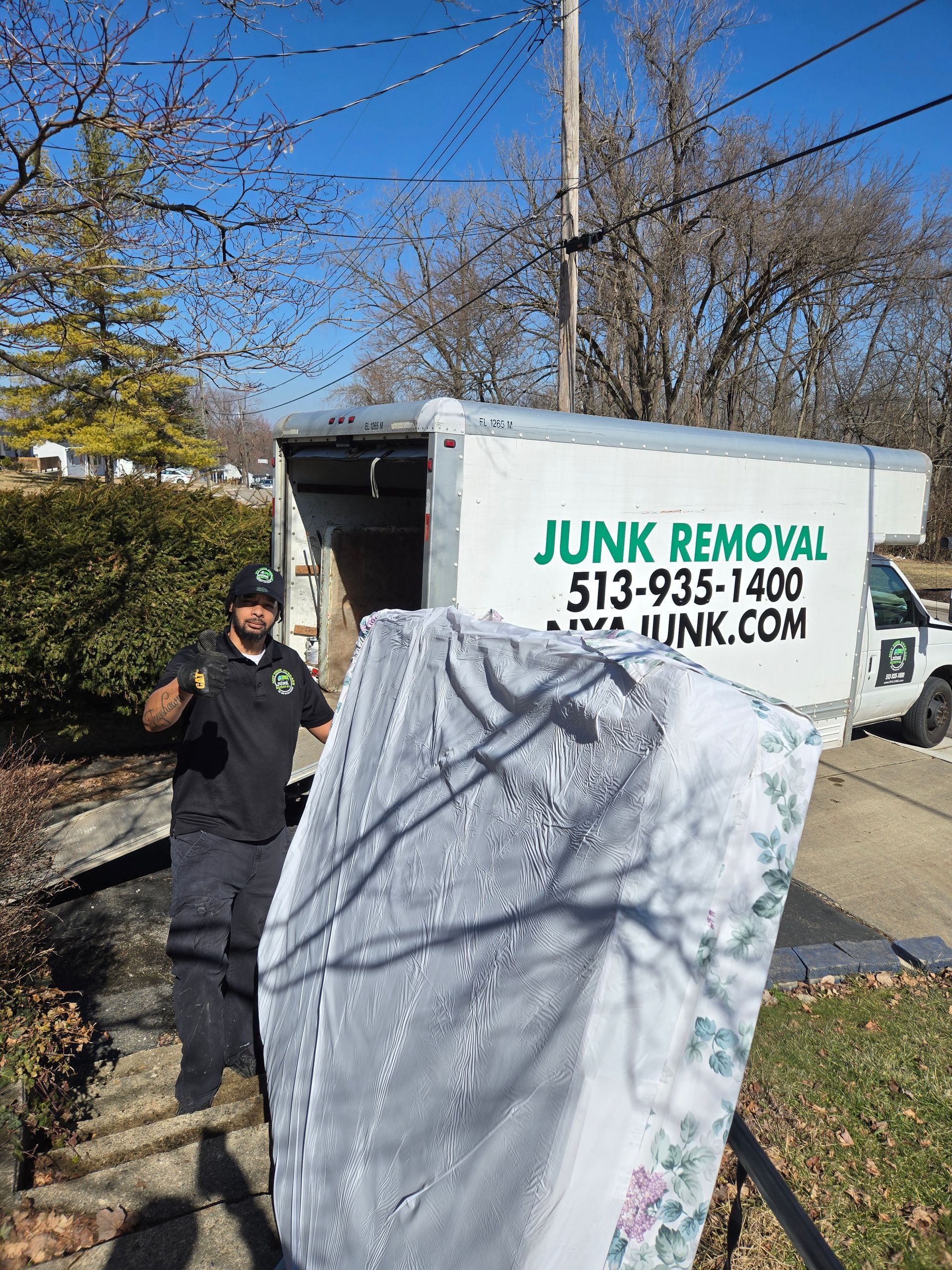 A man is holding a mattress in front of a junk removal truck.