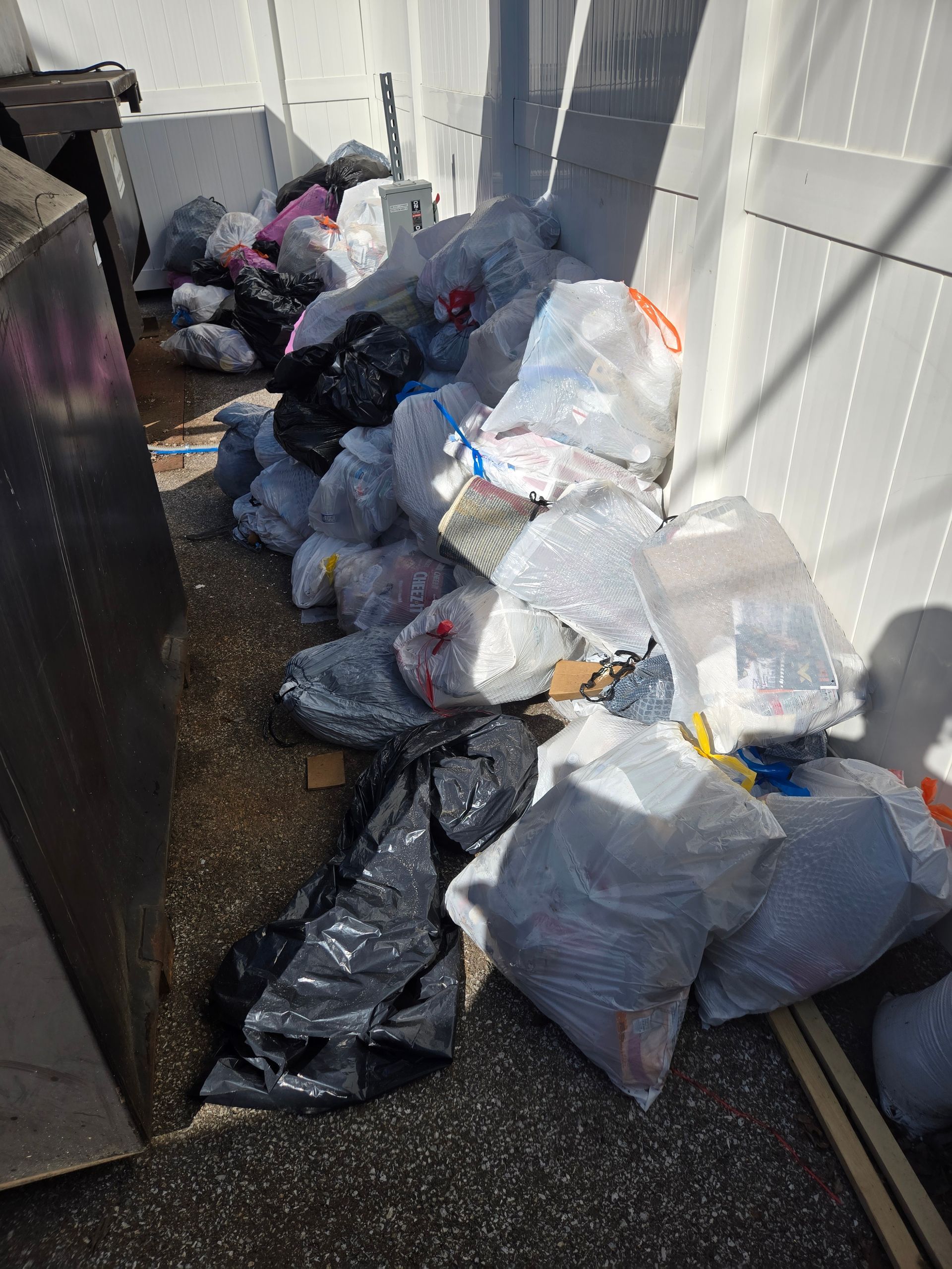 A pile of trash bags sitting on the ground next to a white fence.