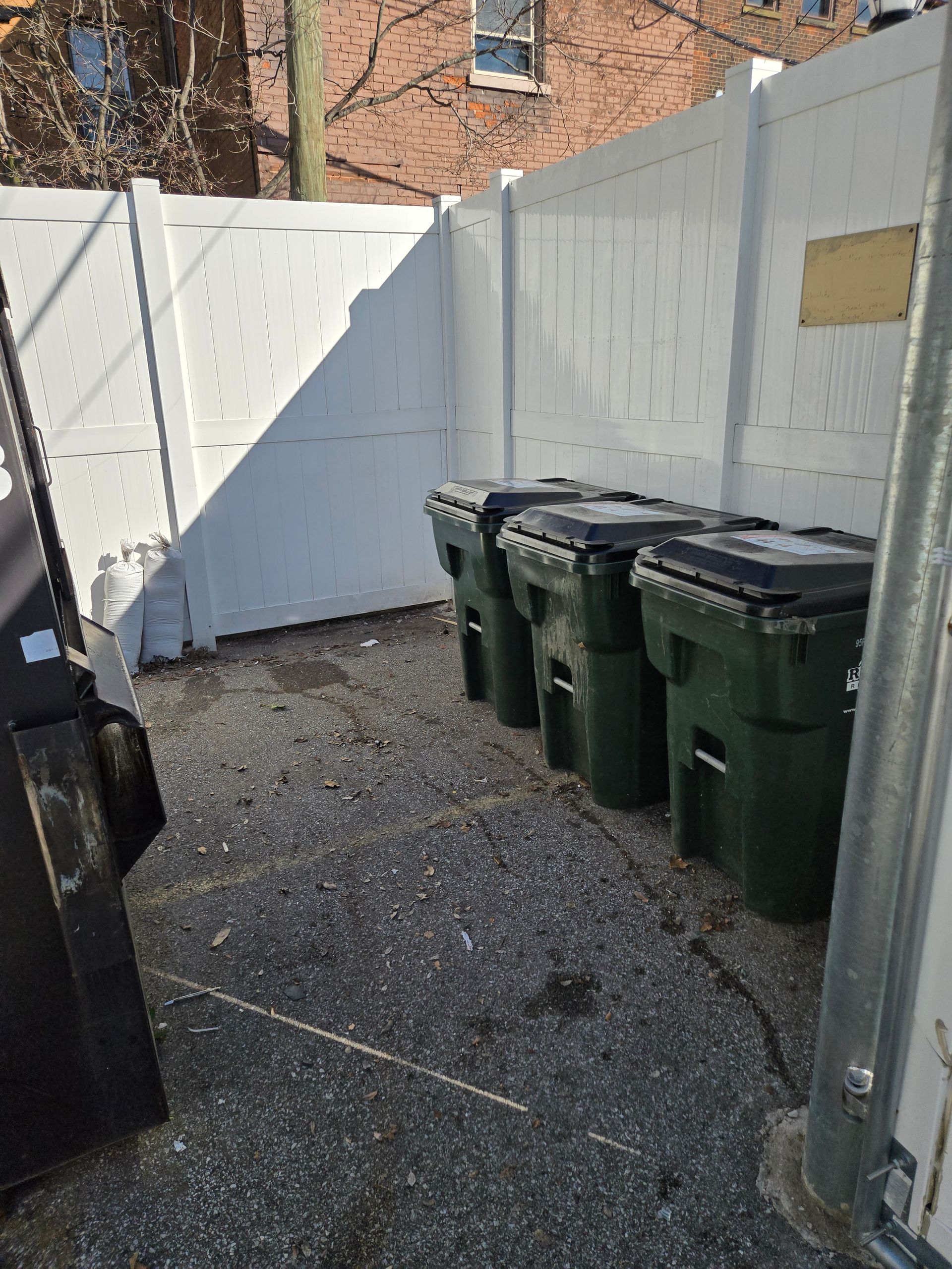 A row of trash cans are lined up in front of a white fence.