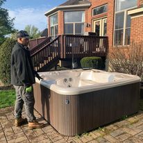 A man is standing next to a hot tub in front of a brick house.