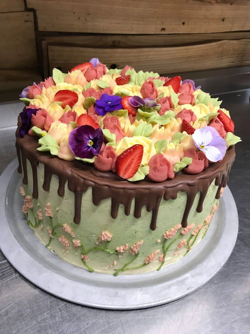 Birthday cake with white icing, chocolate drips and flowers decorating the top