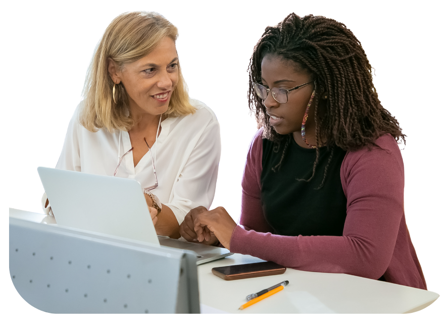 Two women at a table, looking at a laptop. One woman points at the screen while the other smiles.