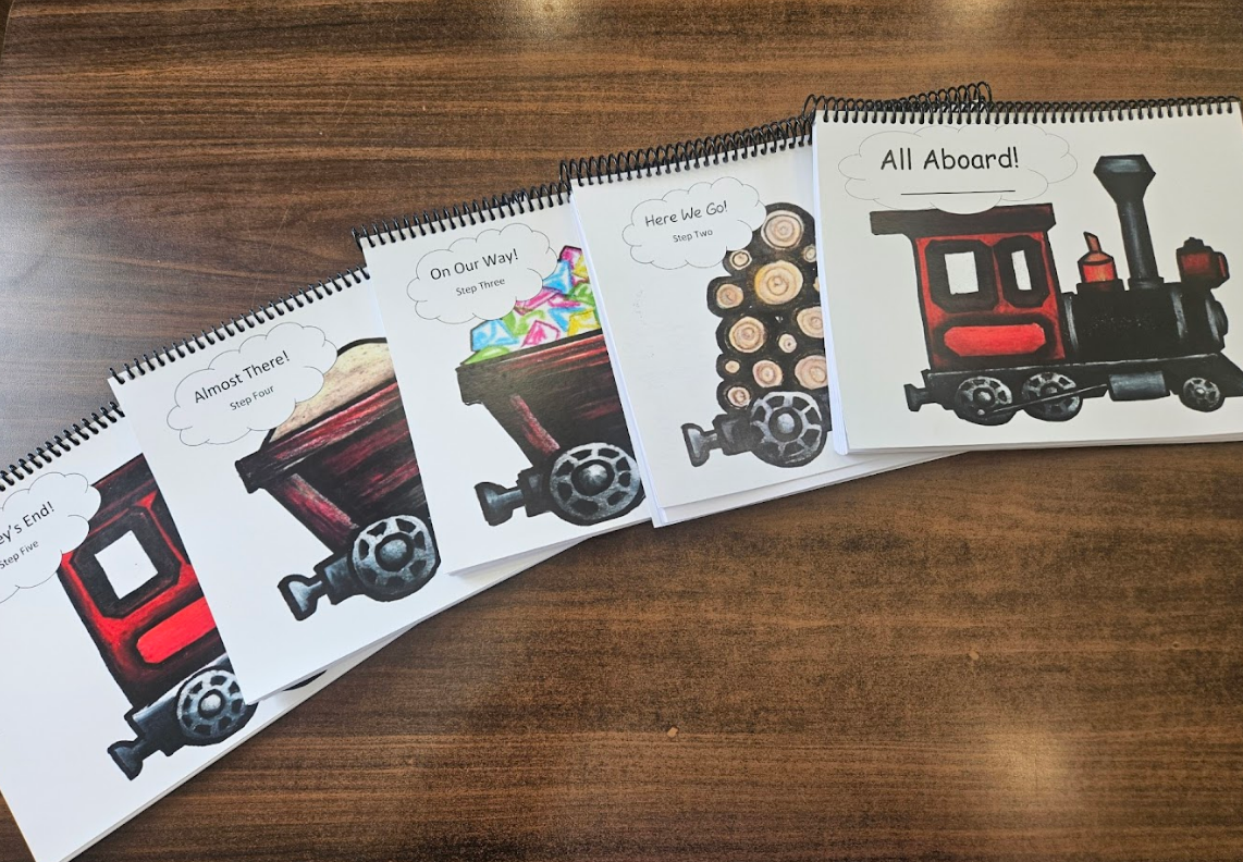 Children's book covers with a train theme on a wooden surface. Red and black train illustrations.