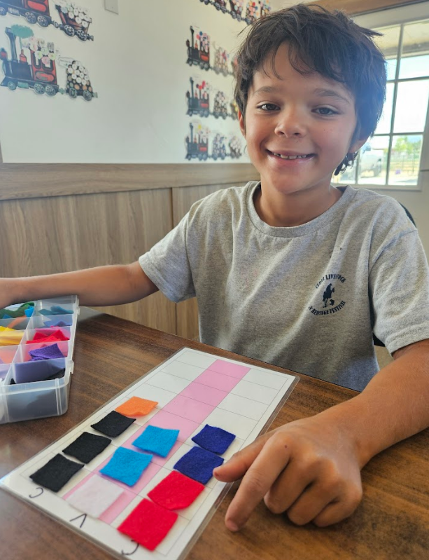 Boy smiles while using colorful squares to learn on a table.