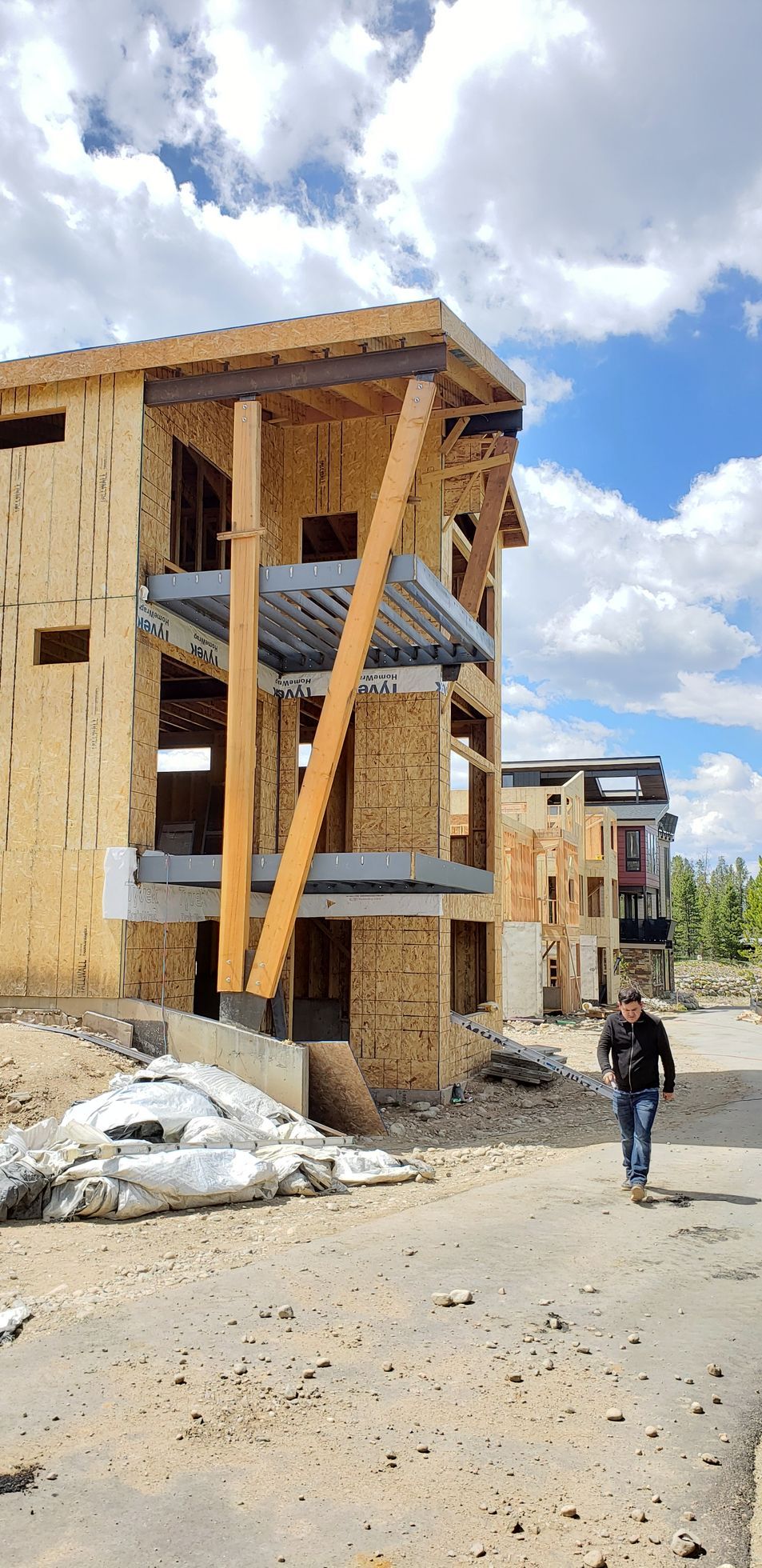 A man is walking down a dirt road in front of a building under construction.