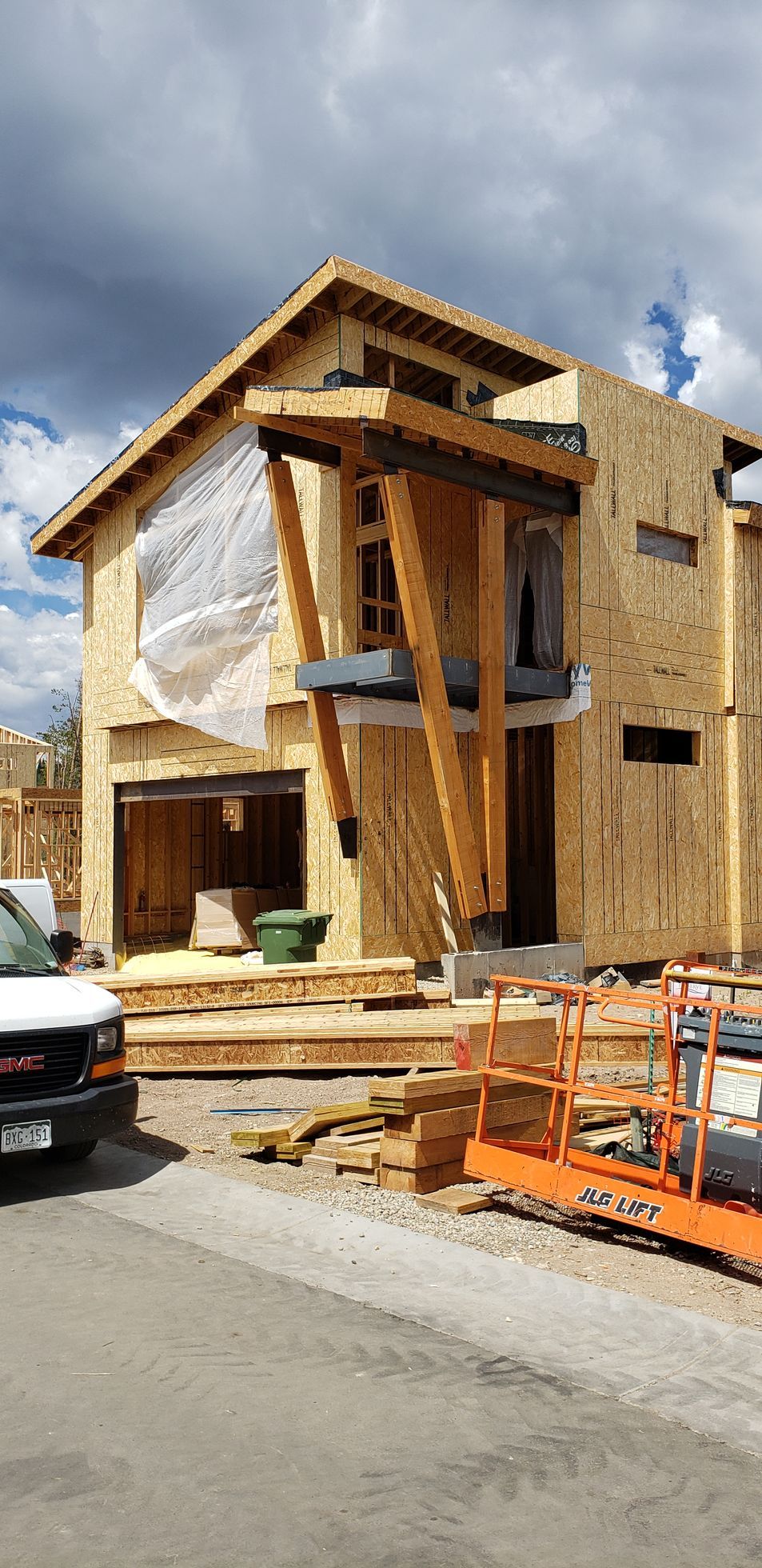A white van is parked in front of a wooden house under construction.