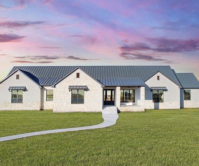 A large white house with a blue roof is sitting on top of a lush green field.