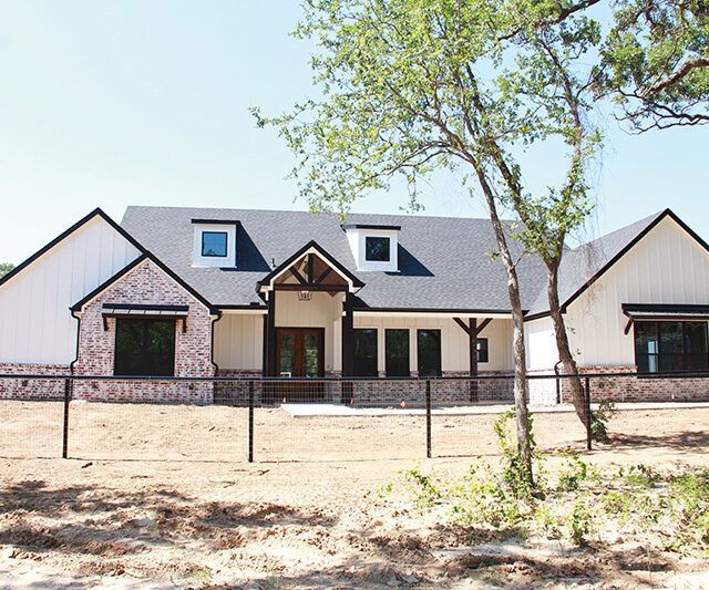 A white house with a black roof and a fence around it