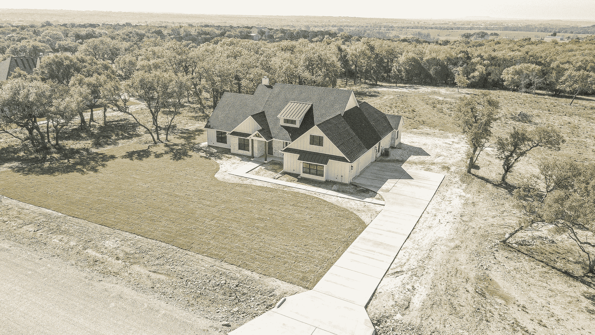 An aerial view of a house with a driveway leading to it surrounded by trees.