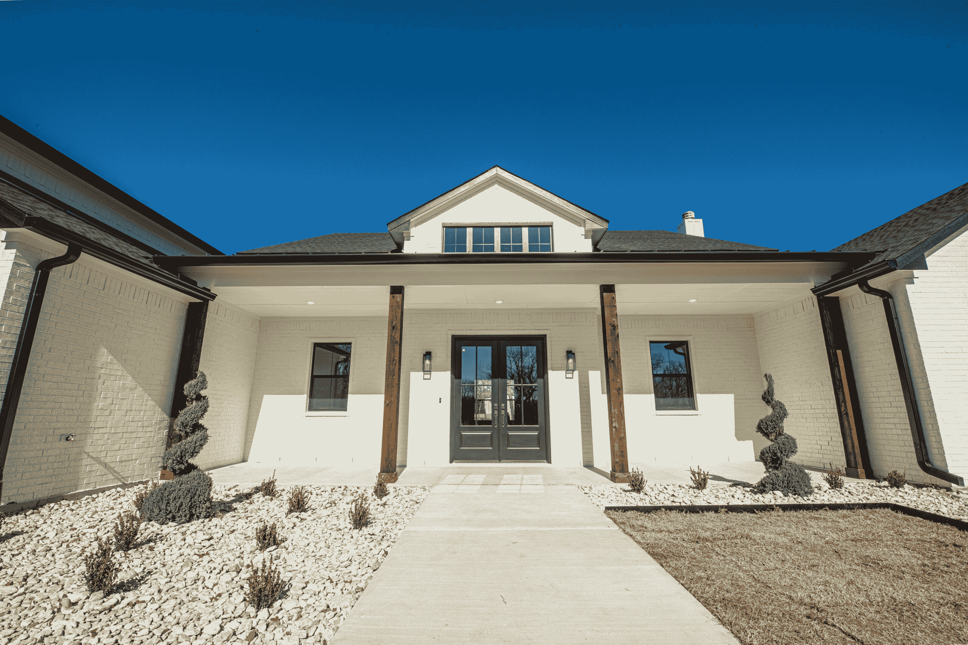 A large white house with a large porch and a blue sky in the background.