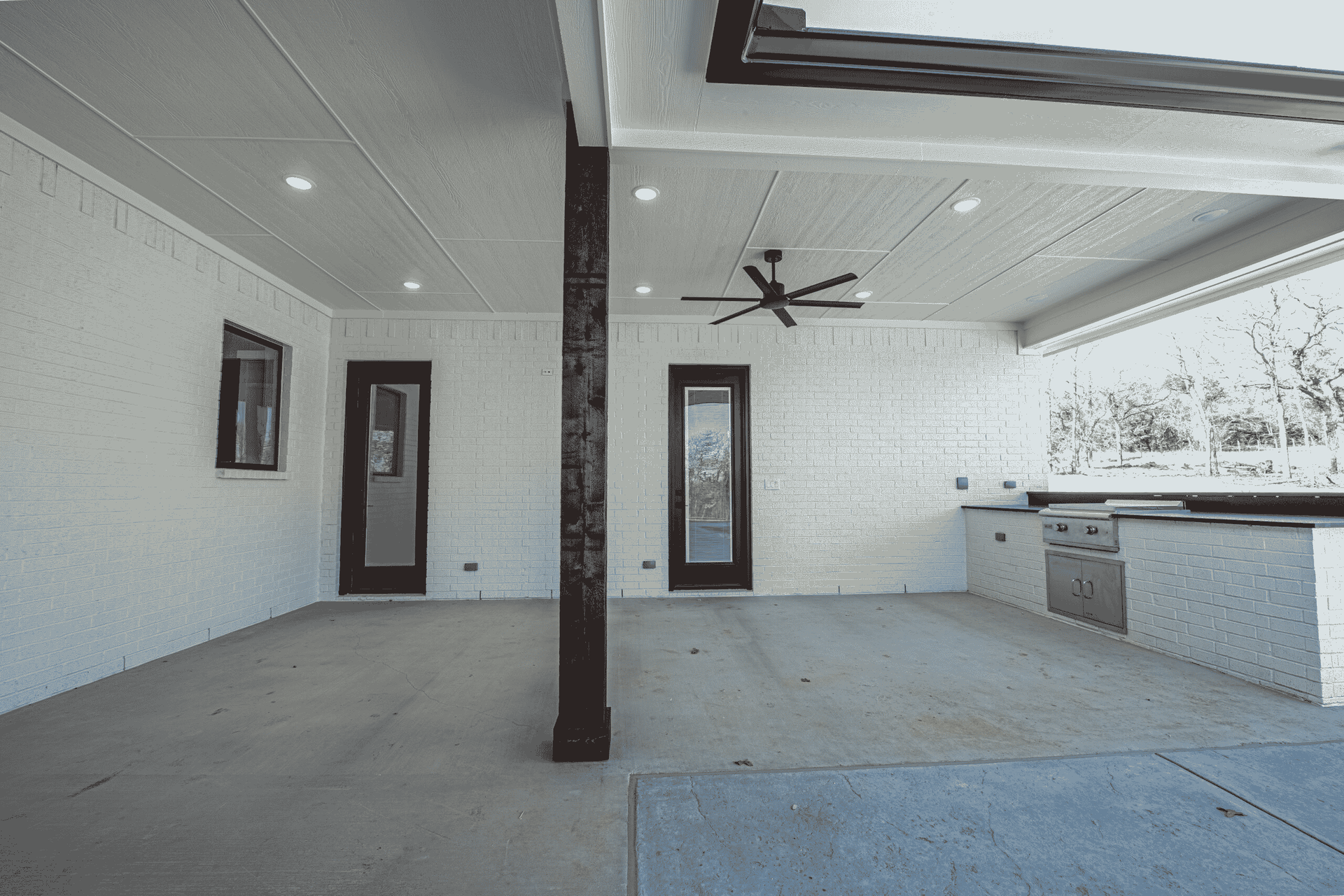 An empty patio with a ceiling fan and a kitchen.