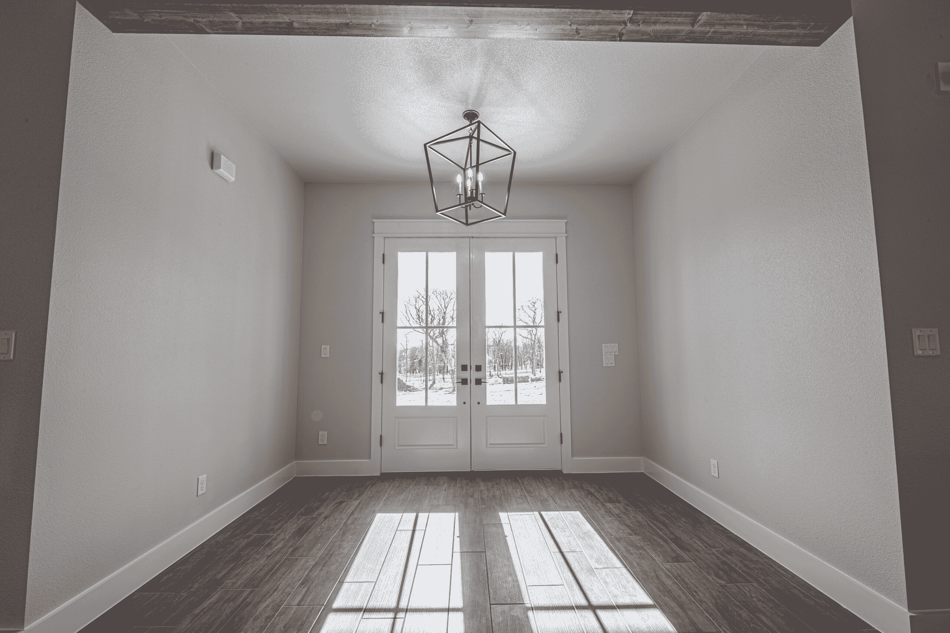 A black and white photo of an empty room with a chandelier hanging from the ceiling.