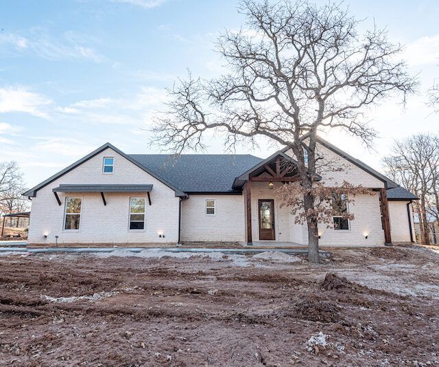 A white house with a black roof and a tree in front of it