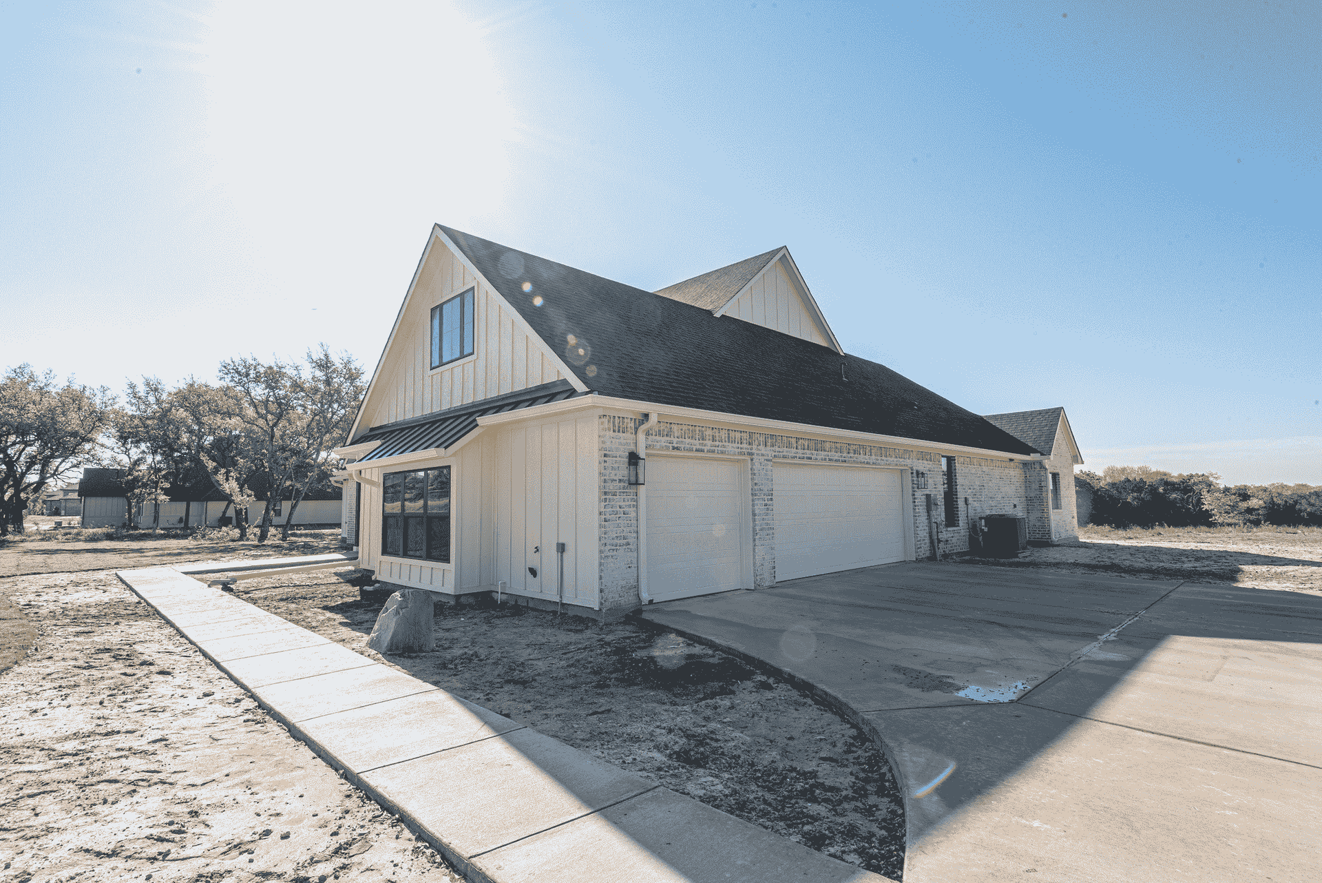 A white house with a black roof is sitting on top of a dirt field.
