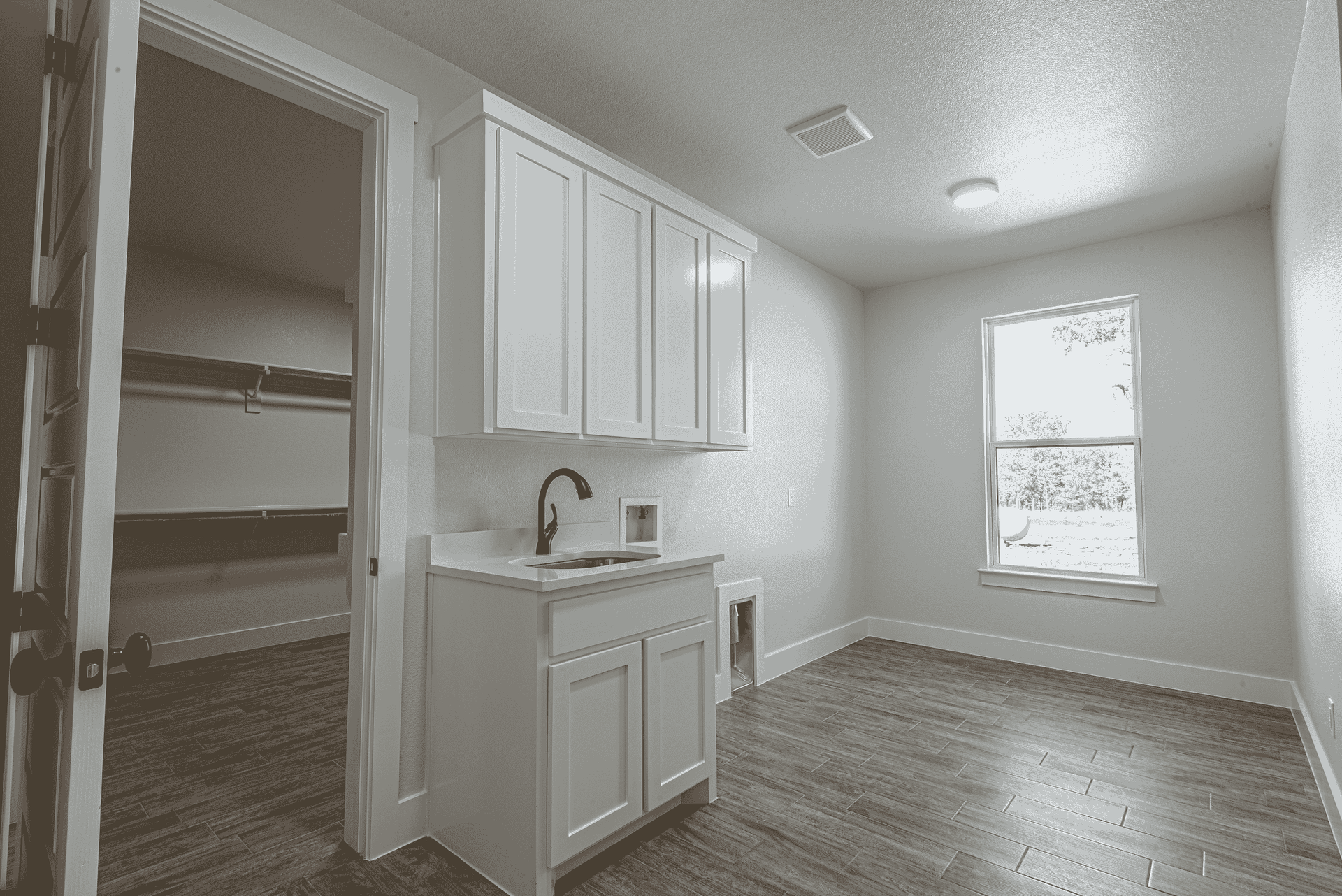 A black and white photo of an empty room with a sink and cabinets.