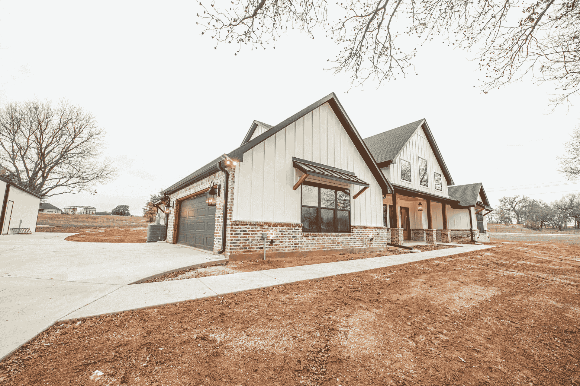 A large white house with a black roof is sitting on top of a dirt field.