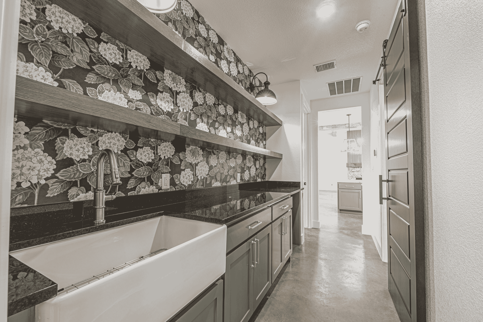 A black and white photo of a kitchen with a sink and shelves.