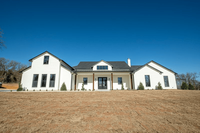 A large white house is sitting on top of a dry grass field.