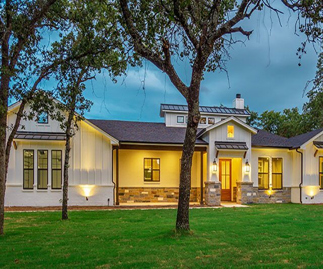 A large white house with a black roof is sitting on top of a lush green field.