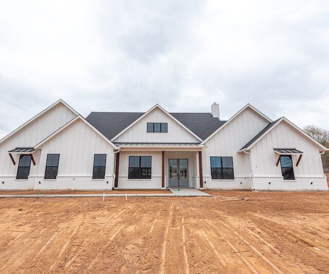A large white house with a black roof is sitting on top of a dirt field.